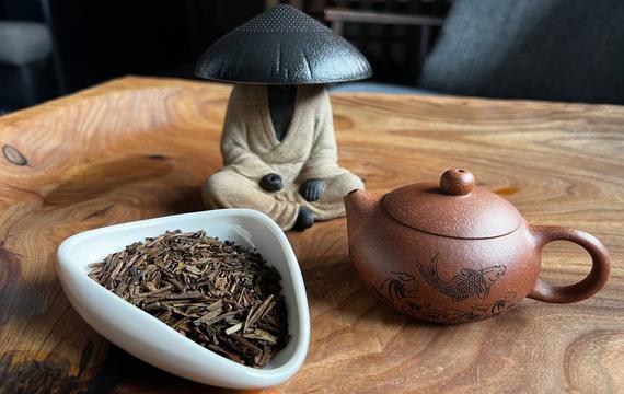 Японский чай ходзича в пиале, рядом исинский чайник с рисунком карпа и фигурка в шляпе-сито на деревянном столе